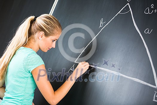 Pretty young elementary school/college teacher writing on the chalkboard/blackboa rd during a math class (color toned image; shallow DOF)