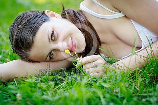 Close-up portrait of an attractive young woman outdoors, lying in the grass, relaxing