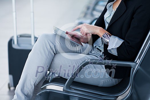 Young female passenger at the airport, using her tablet computer while waiting for her flight (color toned image)