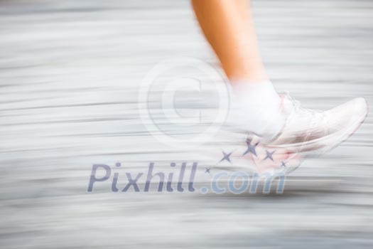 Motion blurred runner's feet in a city environment - running marathon (panning technique used -> motion blurred image; color toned image)