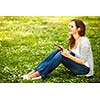 Young woman using her tablet computer while relaxing outdoors in a park on a lovely spring day