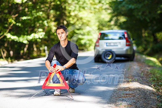 Handsome young man with his car broken down by the roadside, setting the safety triangle