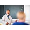 Senior chemistry professor giving a lecture in front of classroom full of students (shallow DOF; color toned image)