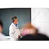 Senior chemistry professor giving a lecture in front of classroom full of students (shallow DOF; color toned image)