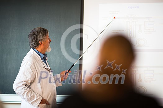 Senior chemistry professor giving a lecture in front of classroom full of students (shallow DOF; color toned image)