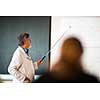 Senior chemistry professor giving a lecture in front of classroom full of students (shallow DOF; color toned image)