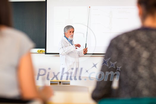 Senior chemistry professor giving a lecture in front of classroom full of students (shallow DOF; color toned image)