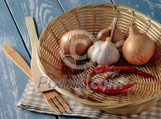 Basket with onions, garlic and red pepper on a wooden table. Basket with onions, garlic and red pepper on a wooden table.