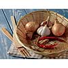 Basket with onions, garlic and red pepper on a wooden table.