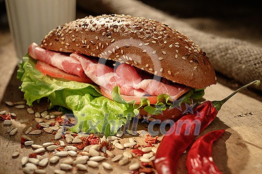 Sandwich on a wooden table with slices of bacon, lettuce and tomatoes.