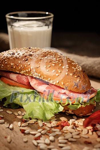 Sandwich on a wooden table with slices of bacon, lettuce and tomatoes.