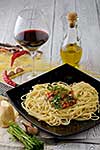 Italian pasta cooked in a rustic style with a sauce of fresh tomatoes and garlic on a wooden table with a glass of red wine. 