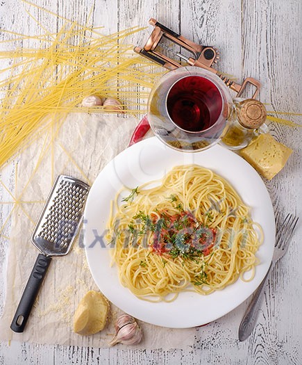 Italian pasta cooked in a rustic style with a sauce of fresh tomatoes and garlic on a wooden table with a glass of red wine. 