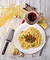 Italian pasta cooked in a rustic style with a sauce of fresh tomatoes and garlic on a wooden table with a glass of red wine. 