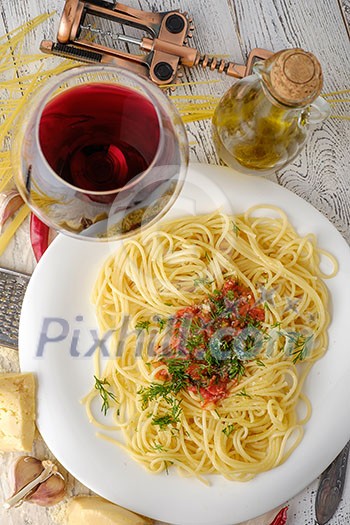 Italian pasta cooked in a rustic style with a sauce of fresh tomatoes and garlic on a wooden table with a glass of red wine. Top view.