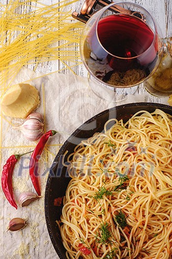 Spaghetti Pasta in airon frying pan with garlic, tomatoes and spices. On the wooden table with red wine and olive oil. Top view.
