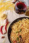 Spaghetti Pasta in airon frying pan with garlic, tomatoes and spices. On the wooden table with red wine and olive oil. Top view.