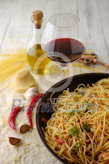 Spaghetti Pasta in airon frying pan with garlic, tomatoes and spices. On the wooden table with red wine and olive oil.
