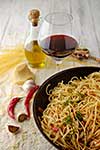 Spaghetti Pasta in airon frying pan with garlic, tomatoes and spices. On the wooden table with red wine and olive oil.