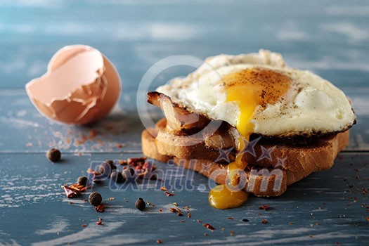 Breakfast - sandwich with fried egg and bacon over blue wooden table Breakfast - sandwich with fried egg and bacon over blue wooden table