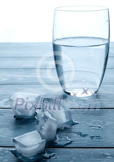 Glass of water and melting ice cubes on a wooden table Glass of water and melting ice cubes on a wooden table