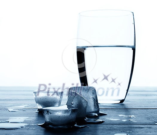Glass of water and melting ice cubes on a wooden table