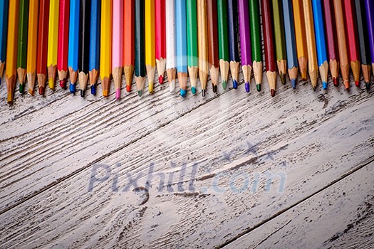 Colored pencils in a row on wooden background