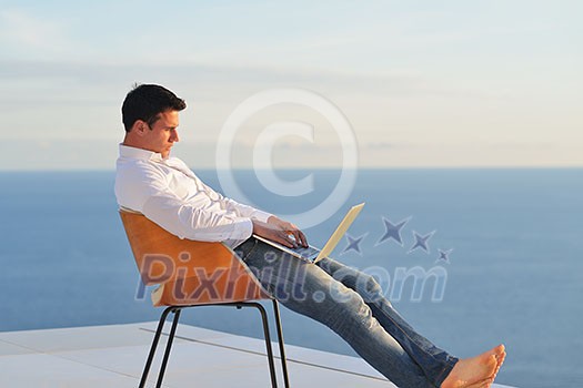 handsome young man relaxing and working on laptop computer at home balcony while looking sunset
