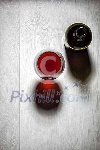 Glass and bottle of red wine with cork on white wooden table. Top view