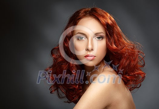 Portrait of a young ginger woman on a dark background. Low key. Long Curly Red Hair. 