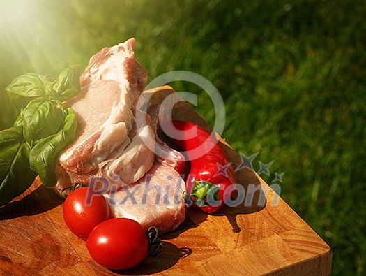 Raw pork steaks on wooden table with tomatoes, peppers and basil.
