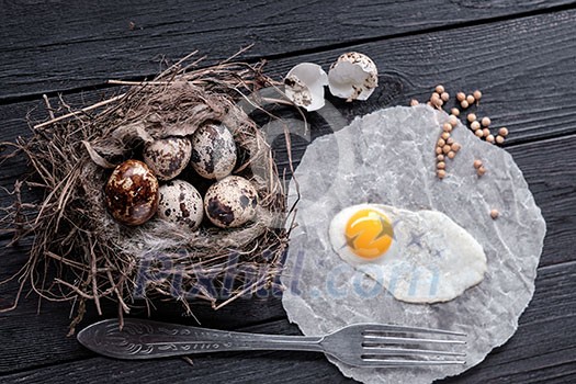 Quail eggs in the nest and a fried egg on a wooden board