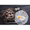 Quail eggs in the nest and a fried egg on a wooden board