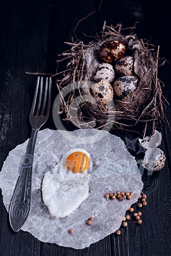 Quail eggs in the nest and a fried egg on a wooden board