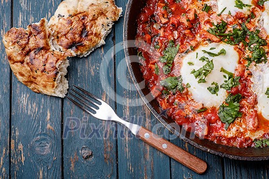 Fried eggs in a frying pan with tomatoes, sausage and greens.