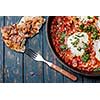 Fried eggs in a frying pan with tomatoes, sausage and greens.