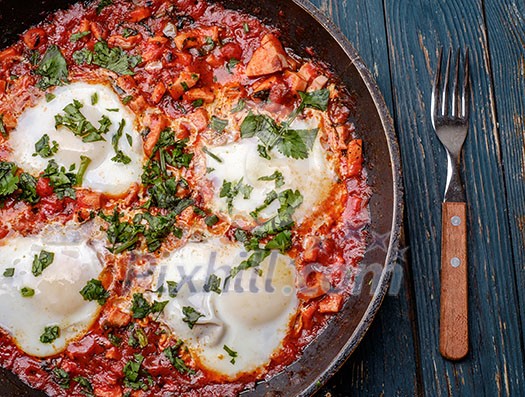 Fried eggs in a frying pan with tomatoes, sausage and greens.