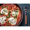 Fried eggs in a frying pan with tomatoes, sausage and greens.