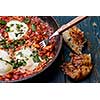 Fried eggs in a frying pan with tomatoes, sausage and greens.