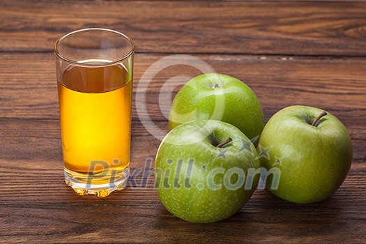 Glass of apple juice and green apples on wooden background