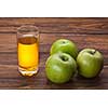 Glass of apple juice and green apples on wooden background