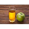 Glass of apple juice and green apple on wooden background