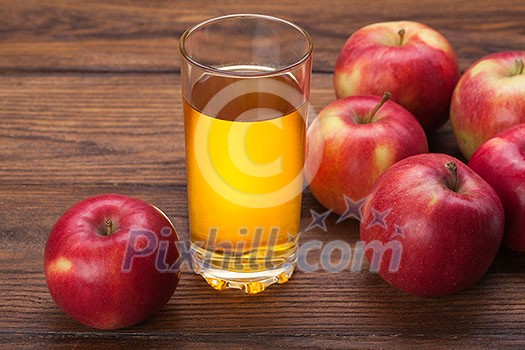 Glass of apple juice and red apples on wooden background