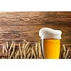 Glass of beer with wheat on wooden background