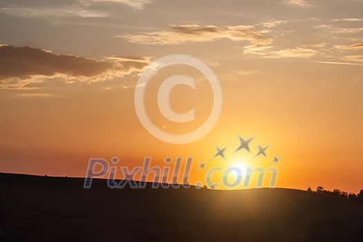 Silhouette of hill on sunset with sun and clouds