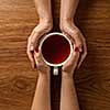 Womans and mens hands holding hot cup of tea on wooden table