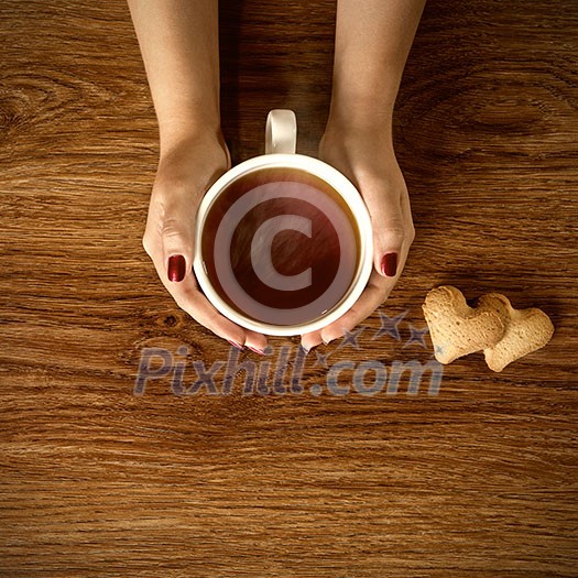 woman holding hot cup of tea with cookies on wooden table woman holding hot cup of tea with cookies on wooden table