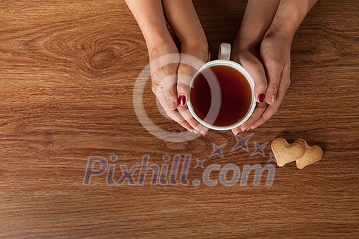 Womans and mens hands holding hot cup of tea on wooden table
