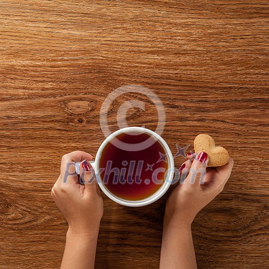 woman holding hot cup of tea with cookies on wooden table woman holding hot cup of tea with cookies on wooden table