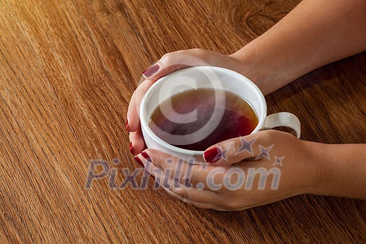 woman holding hot cup of tea on wooden table